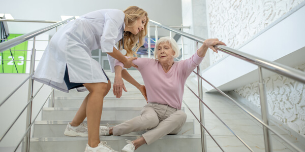 Blonde Nurse Helping The Senior Woman Who Fell Down On The Strairs